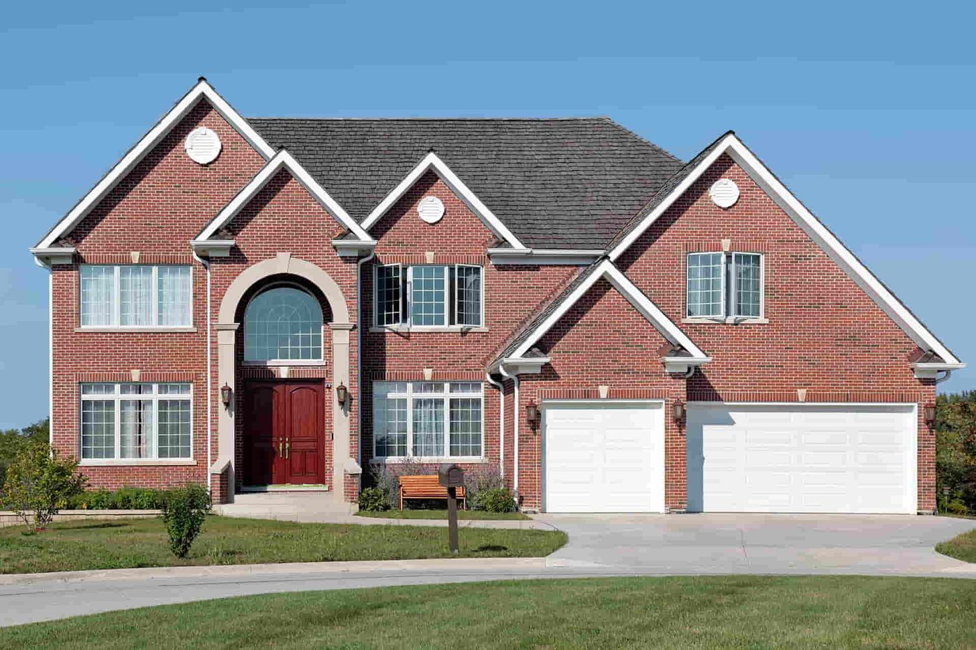 Large red brick home with a shingle roof and a double garage