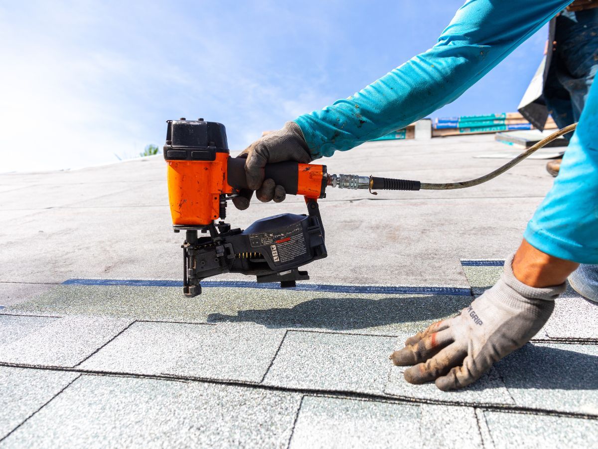 Roofer installing new architectural shingles with a nail gun